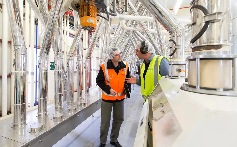 Two workers in high visibility clothing and PPE inside a milk processing plant